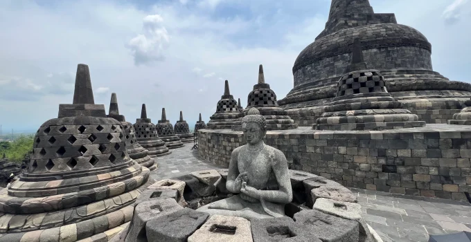 Aerial view of Borobudur Temple surrounded by lush greenery and distant hills.