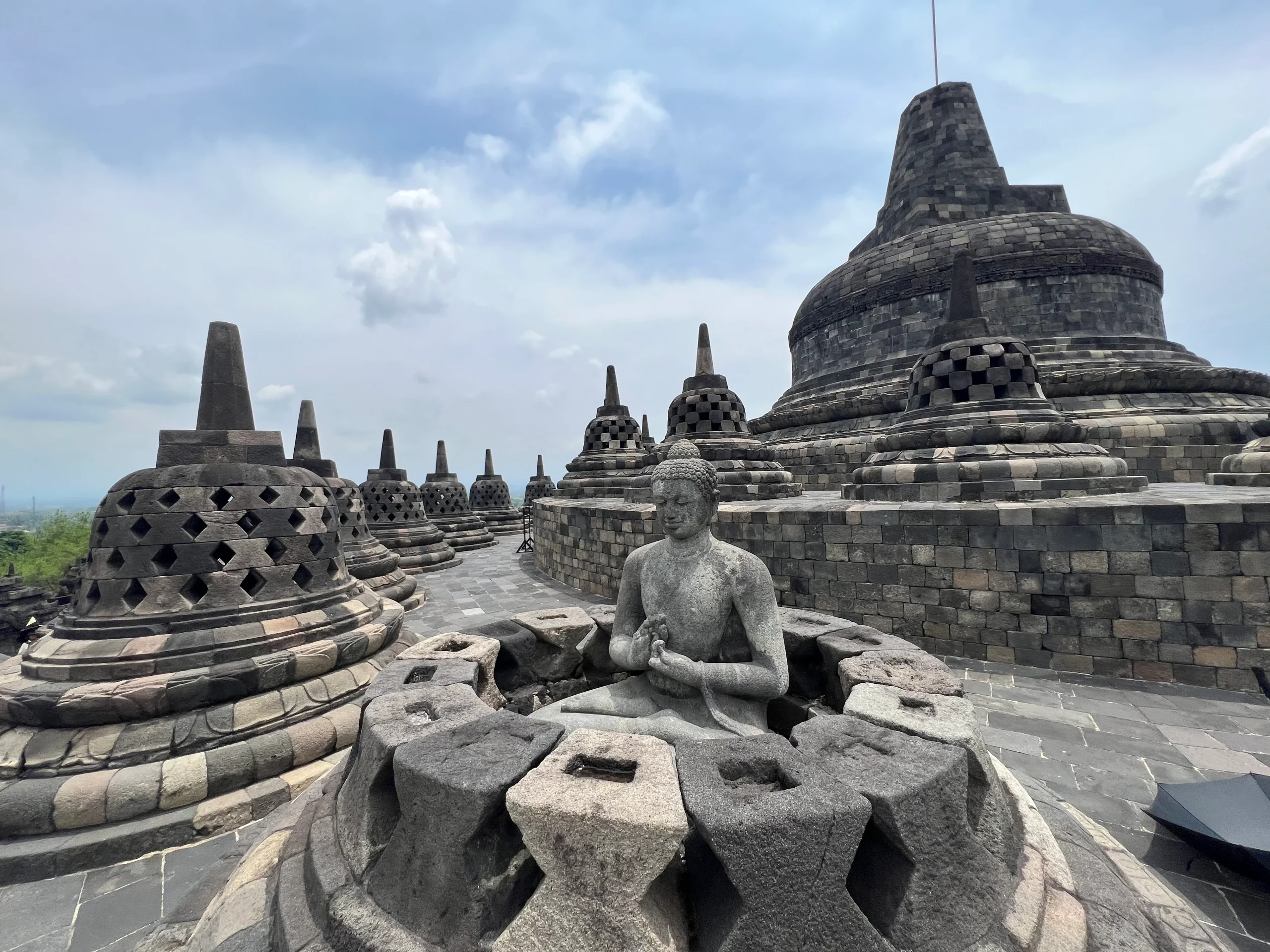 Aerial view of Borobudur Temple surrounded by lush greenery and distant hills. 